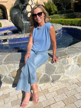 Woman in a blue sleeveless top and jeans sitting by a pool with a fountain in the background.