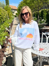 Woman wearing a white sweatshirt with a graphic design, sitting outdoors.