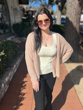 Woman wearing a natural cardigan, white top, and black pants on a sidewalk.