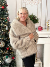 Woman in Beige Artic Faux fur coat standing next to a decorated Christmas tree with a fireplace in the background.