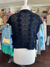 Navy blue knitted short sleeve sweater back view on a mannequin in a store setting with clothing racks in the background.