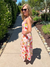 Woman in a picnic print dress standing on a sidewalk with trees and shrubs in the background