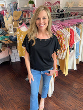 Woman standing in a clothing store wearing a black top and blue jeans.
