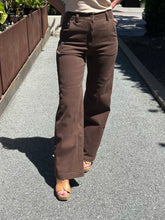 A person wearing brown wide-leg pants and tan wedge sandals walking on a paved outdoor path.