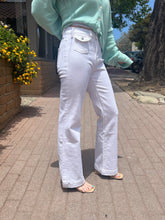 Person wearing a light green cardigan and white pants on a sidewalk.