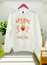 White sweatshirt with Aperol graphic design on a hanger against a light background