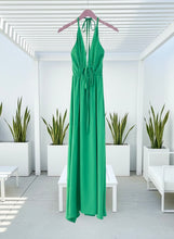 Green halter dress on a hanger against a white background with plants.
