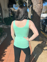 Person wearing a mint tank top and black pants standing outdoors on a sidewalk.