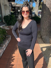 Woman wearing a black long-sleeve top and black pants standing on a sidewalk.