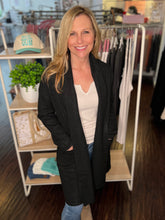 Woman standing in a clothing store wearing a black cardigan and white shirt.