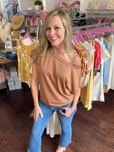 Woman in a clothing store wearing a brown top with studded details and blue jeans.