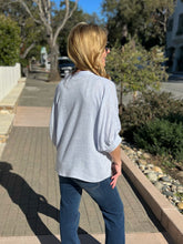 Woman wearing a light blue top and sunglasses outdoors on a sunny day.