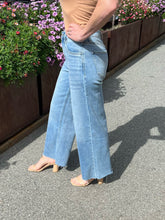Person wearing light blue jeans standing on a pavement with flowers in the background