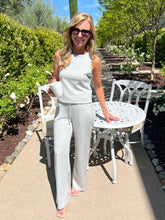 Woman in a light gray outfit standing outdoors near white chairs and tables.