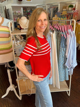 Woman in a red and white striped shirt standing in a clothing store with racks of clothes and accessories.