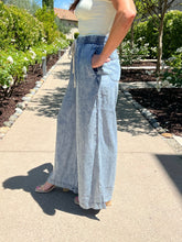 Person wearing light blue wide-leg pants and a white top on a sidewalk.