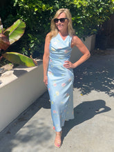 Woman in a light blue floral dress standing outdoors with greenery in the background