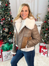 Woman wearing a brown jacket with white fur trim in a festive setting with Christmas trees and presents.