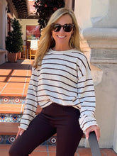 A woman wearing a cream and dark brown horizontally striped knit sweater, dark brown pants, and sunglasses, posing on outdoor terracotta steps.
