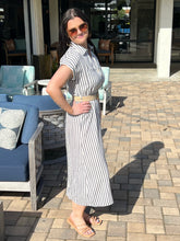 Woman in a striped dress standing on a patio with outdoor furniture.