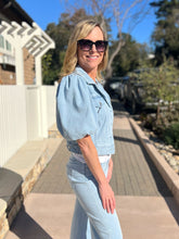 Woman wearing a light blue cropped denim jacket and jeans outdoors on a sunny day.