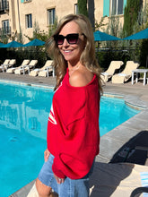 Woman in a red shirt and sunglasses standing by a poolside.