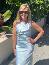 Woman in a light blue floral top standing outdoors with greenery in the background