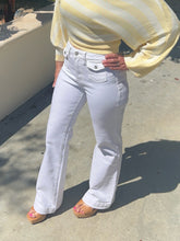 Person wearing a yellow oversized shirt and white jeans on a concrete surface.