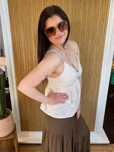 Woman wearing a white top and brown skirt standing in front of a wooden wall.