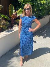 Woman in a blue dress standing outdoors with plants in the background