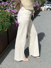 Person wearing natural drawstring jeans standing on a pavement with flowers in the background
