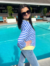 Woman in a blue and white striped shirt and jeans standing by a pool.