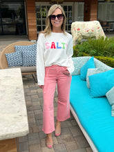Woman wearing a 'SALT' sweatshirt and pink pants standing outdoors.
