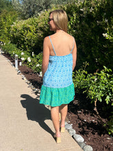 Woman in a blue and green dress walking along a garden path.