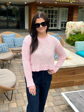 Woman in pink sweater and sunglasses standing in front of a building with outdoor seating area.