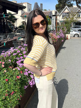 Woman in a yellow striped sweater standing next to flowers with a scenic background