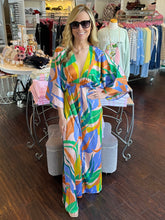 A woman wearing a bold print kimono maxi standing in a store by a display.