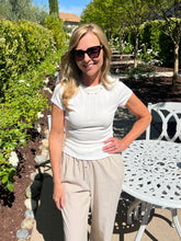 Woman in a white top and beige pants standing in a garden setting.