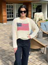 Woman wearing a sweater with an American flag design outdoors.