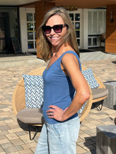 Woman wearing sunglasses and a blue tank top standing outdoors on a patio.