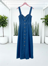 Dark Chambray dress on a hanger against a white wall with plants in the background