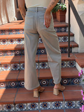 A person wearing light beige wide-leg cropped jeans and beige block-heel sandals, standing on outdoor terracotta tile stairs with patterned blue and white tiles.