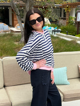 Woman in a striped sweater and sunglasses standing outdoors on a patio.