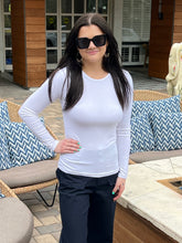 Woman wearing a white long-sleeve top and dark pants outdoors.