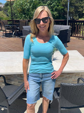 Woman wearing sunglasses and a blue shirt standing outdoors on a patio.