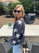 Woman wearing a navy sweater with white star patterns outdoors on a patio.