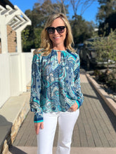 Woman wearing a blue and teal patterned blouse and sunglasses outdoors.