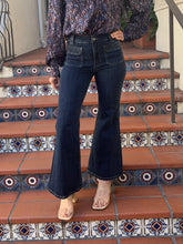 A person wearing dark blue high-waisted flare jeans, a patterned long-sleeve blouse, and clear high-heel sandals, standing on terracotta tiled stairs with decorative blue and white mosaic tiles.