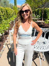 Woman in a white outfit with sunglasses standing outdoors near a garden.