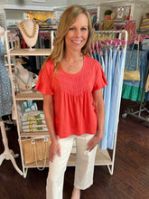 Woman in a red top and white pants standing in a clothing store.